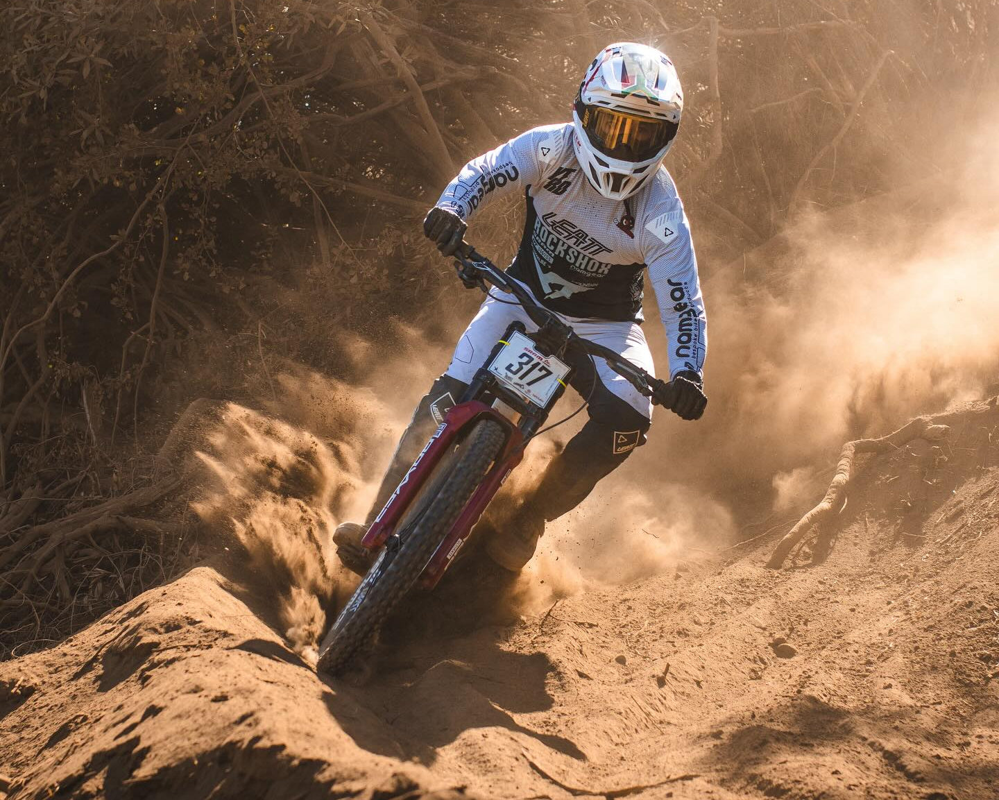 Biker in action on a dirt track with dust and trees in the background