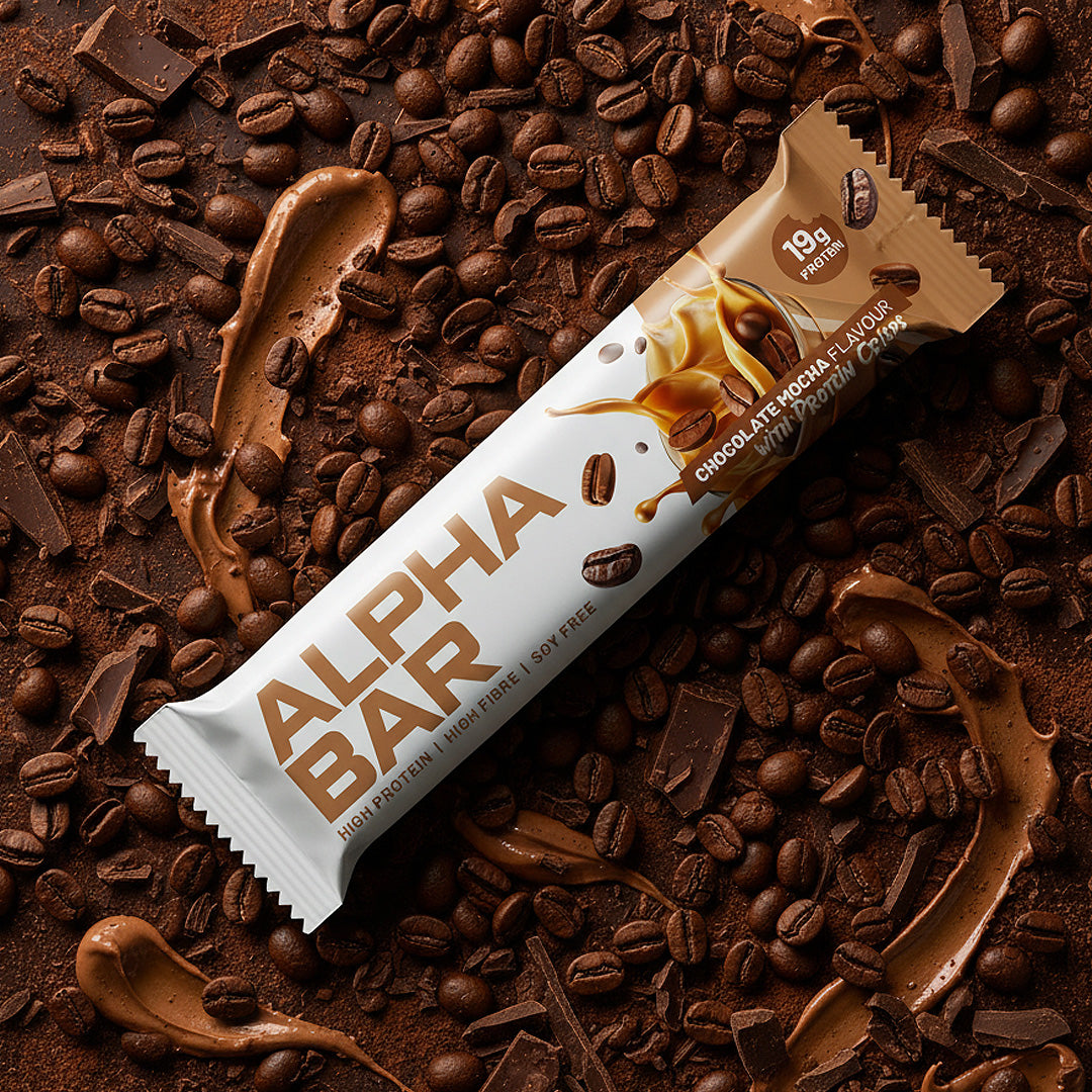 Alpha Bar chocolate protein bar surrounded by coffee beans and chocolate pieces on a brown background