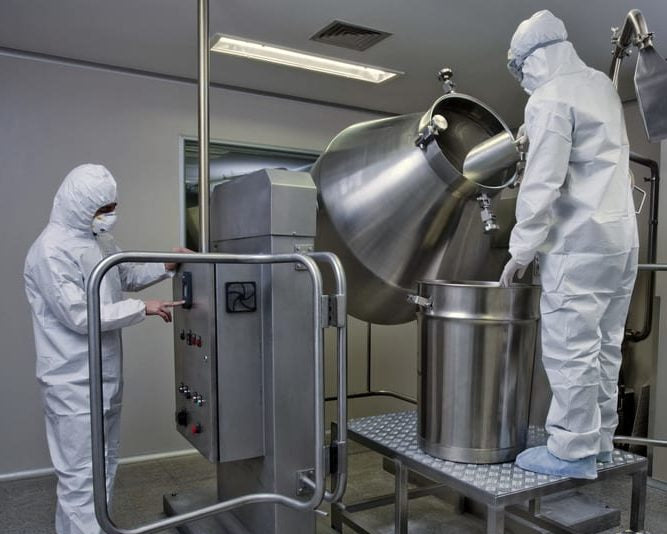 Two people in white protective suits working with large industrial equipment in a controlled environment.
