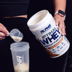 Person measuring Alpha Sports Nutrition Optimal Whey protein powder into a shaker.