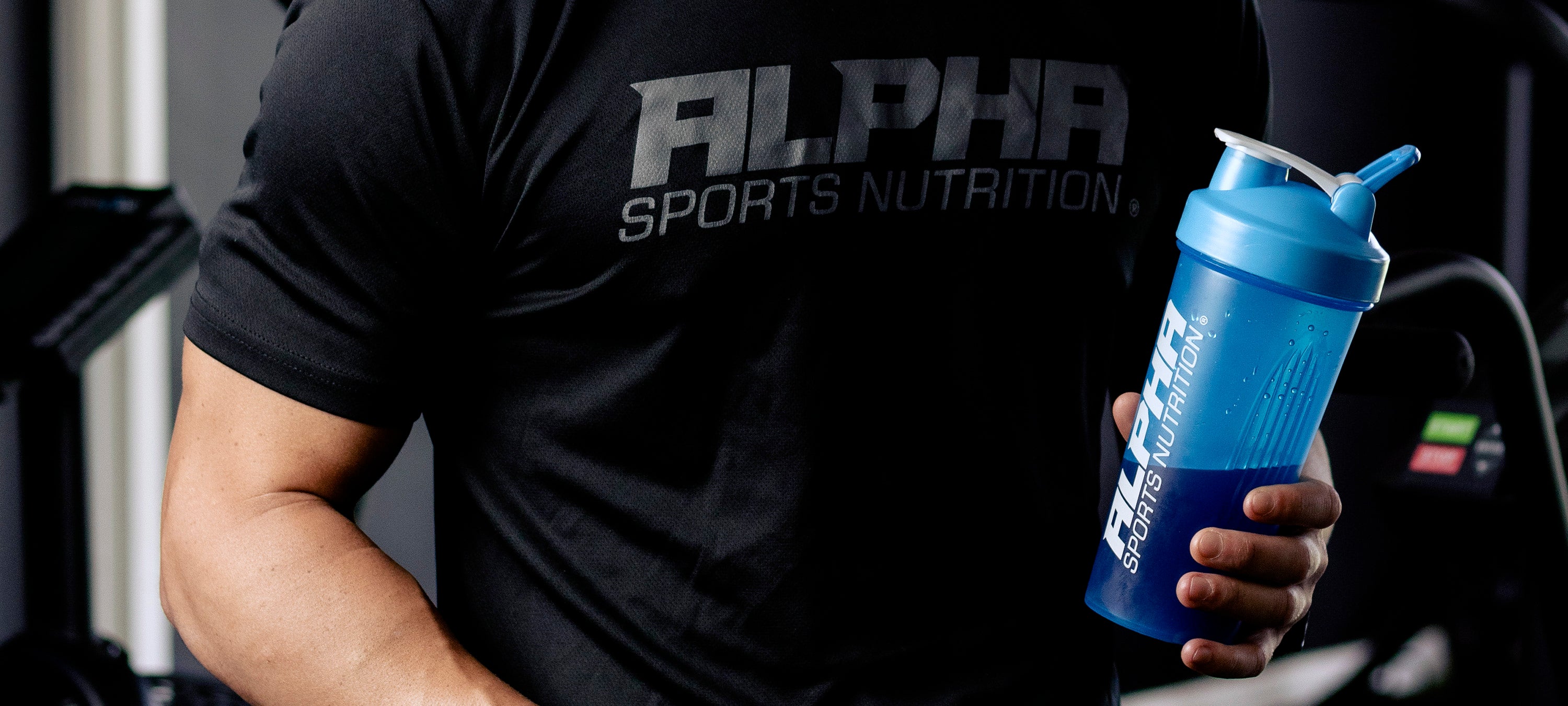 Person wearing an Alpha Sports Nutrition t-shirt holding a blue shaker bottle.