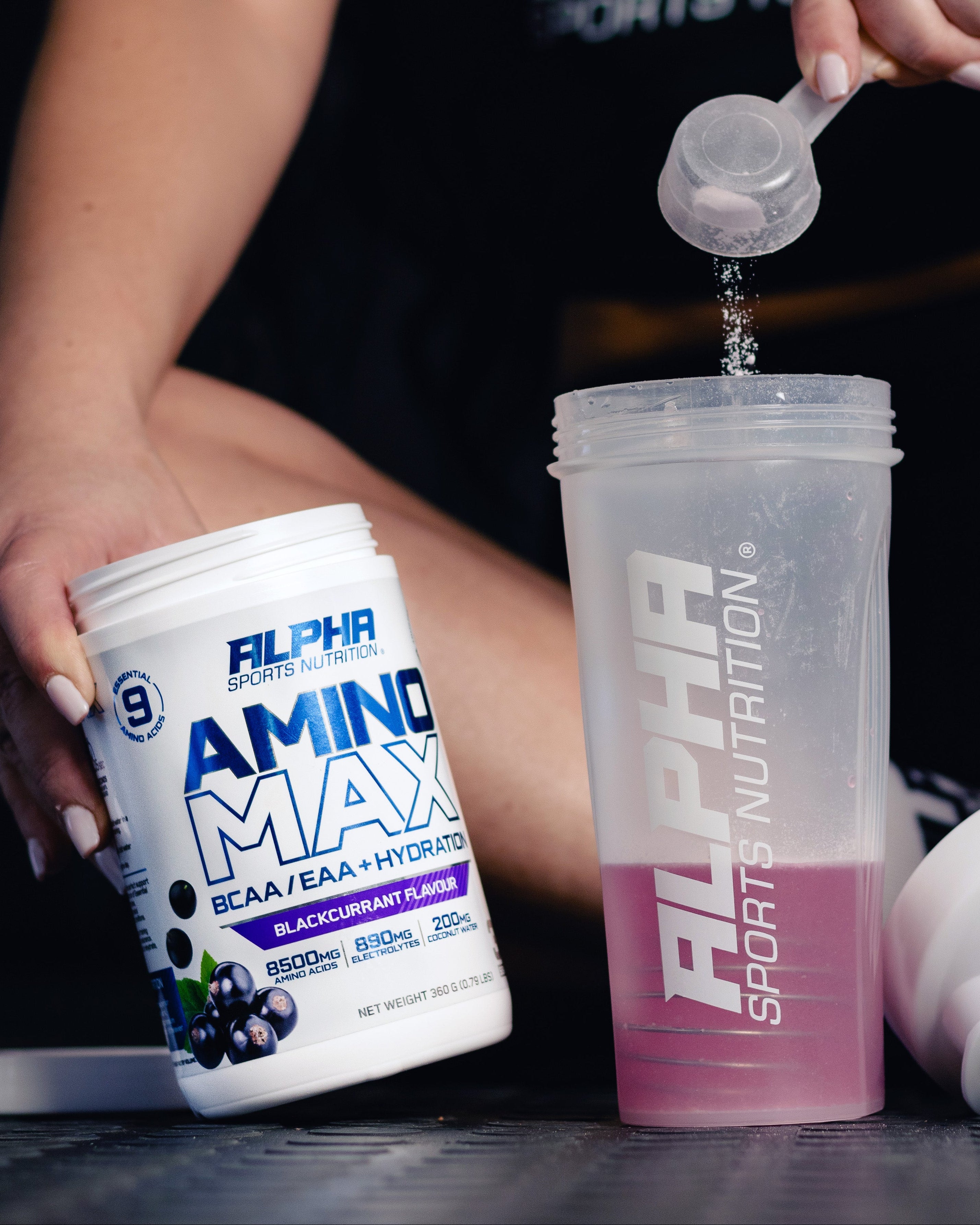Person using Alpha Sports Nutrition Amino Max supplement with a scoop and shaker bottle.