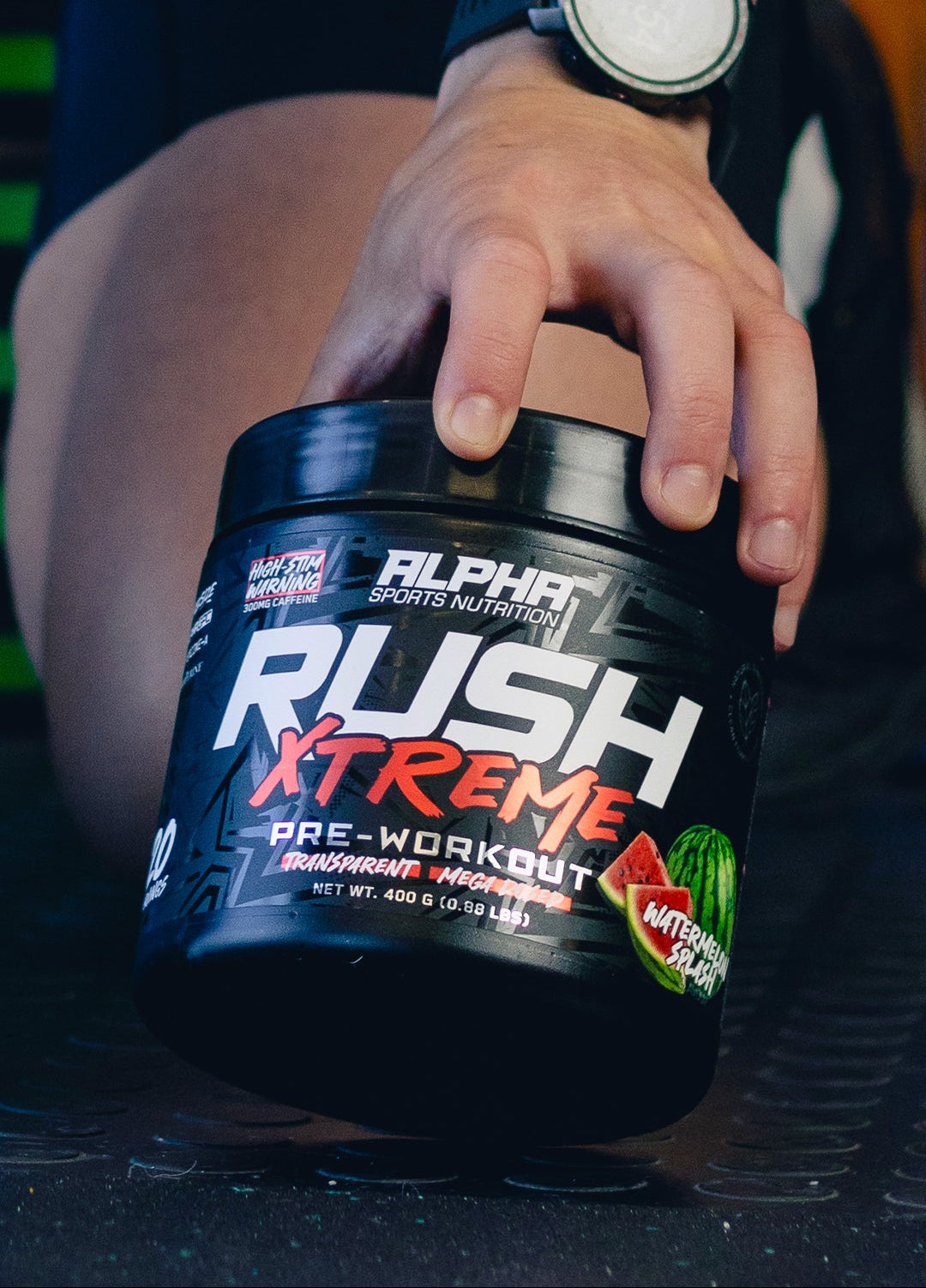 Person holding a container of Alpha Sports Nutrition Rush Xtreme pre-workout supplement.
