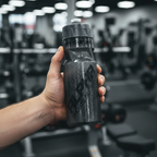 Hand holding a black water bottle with gym equipment in the background